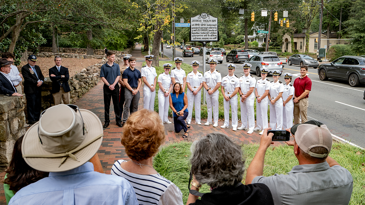 A large group of people, most of whom are Navy ROTC members dressed in white uniforms, posing for a photo in front of a newly unveiled historical marker on the side of Franklin Street.