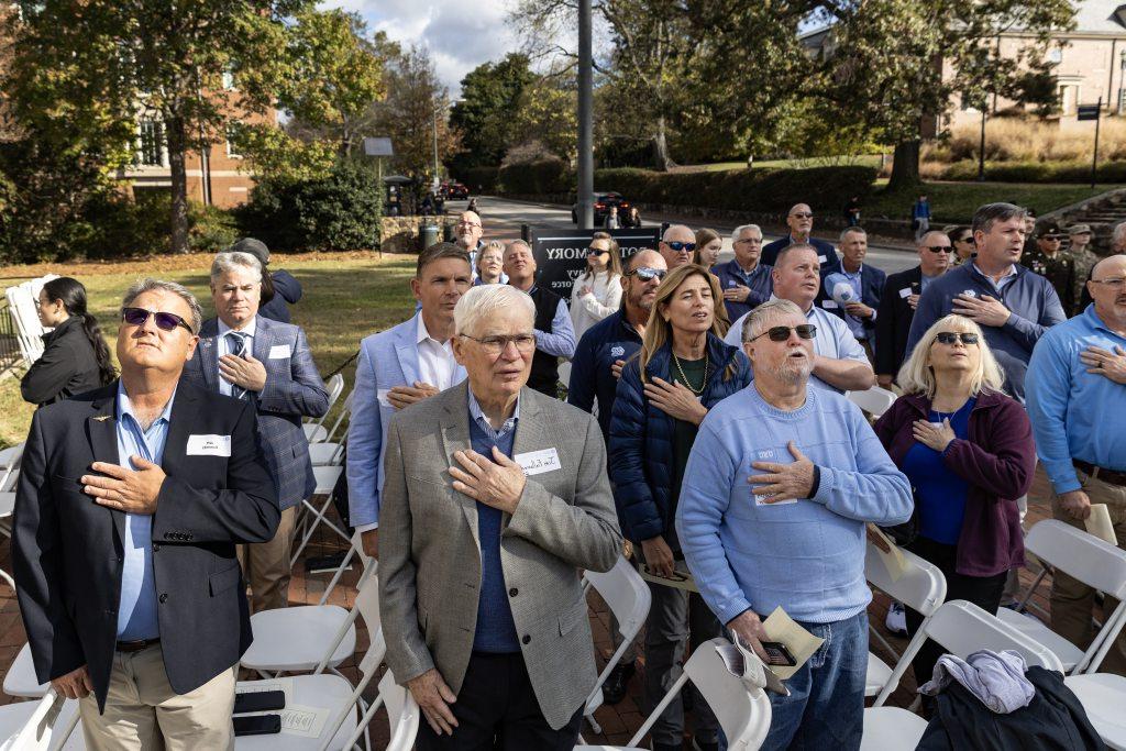 Group of people with their hands of the chest during the playing of the national anthem on the lawn of the Naval ROTC Armory on the campus of UNC-Chapel Hill.